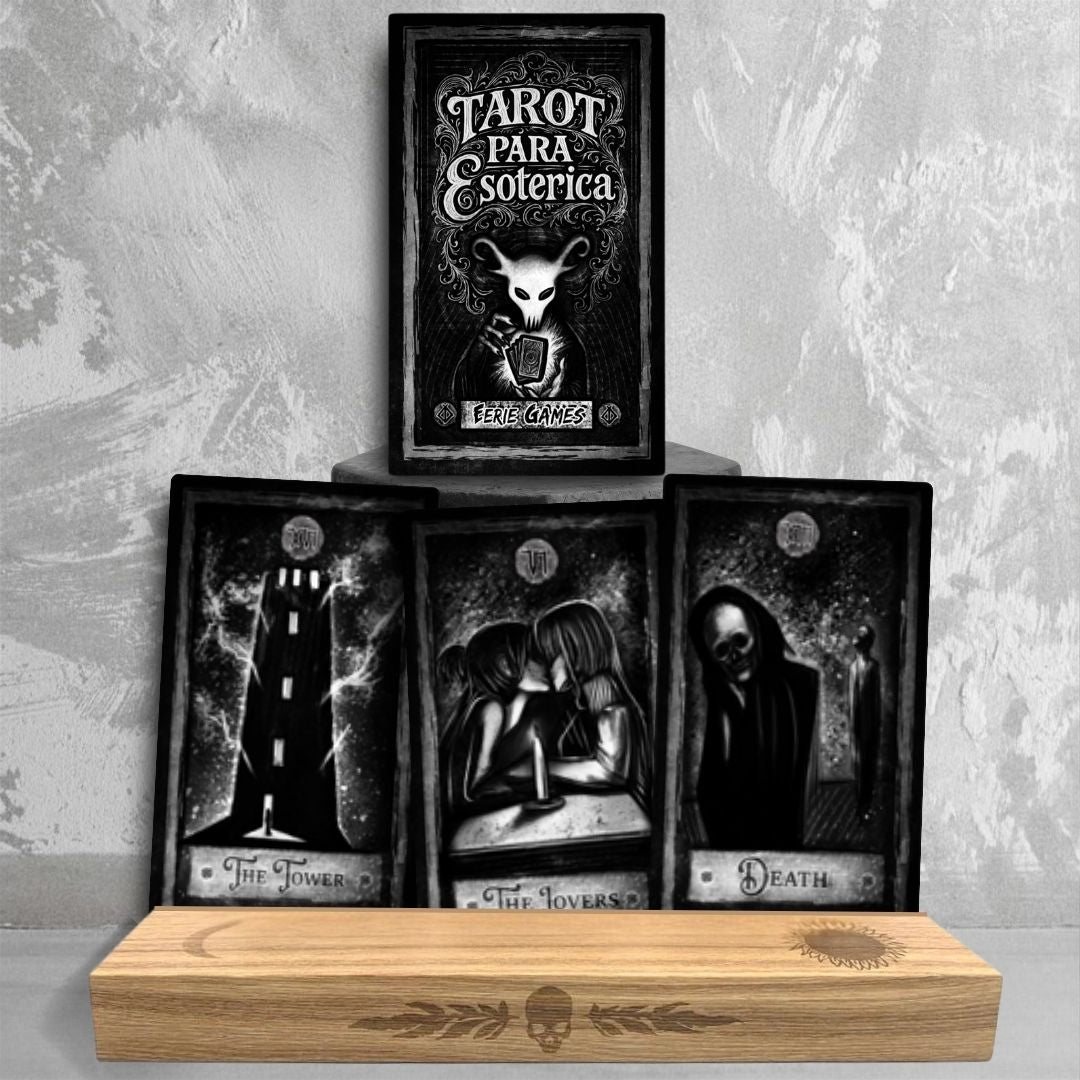 A tarot deck box sits on a stone platform titled the PARA Esoterica Tarot with the White skulled Eerie Games mascot shuffling a deck. Below the box are three upright tarot cards in a stand. They are all stylized in black and white, The Tower card: a flaming black tower with open windows. The Lovers: Two people sharing a kiss over the light of a single candle. Death: A hooded skeletal figure with a person standing behind it.